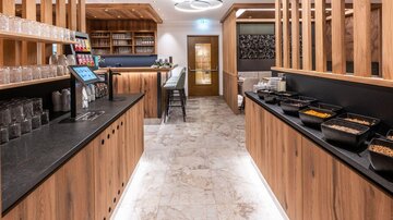 A modern eatery with wood and stone accents. The space is bright and inviting, with a counter that offers various foods.