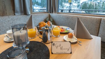 A beautifully set breakfast table with various foods and drinks. In the background, you can see a picturesque mountain landscape.