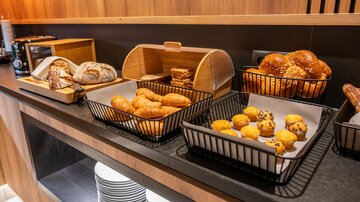 A buffet with various baked goods, including rolls, croissants, and small muffins. The foods are arranged in baskets on a dark table.