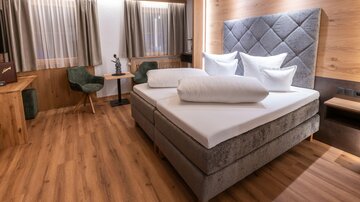 A modern bedroom with a comfortable bed and elegant wood paneling. The cozy atmosphere is enhanced by natural light and stylish furniture.