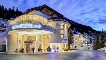 An elegant hotel building with an inviting facade and warm lights. The surroundings showcase a picturesque mountain landscape in the background.