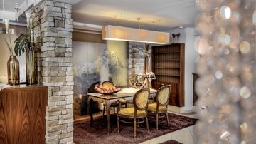 An elegant dining area with a wooden table and cozy chairs. The walls are partially clad with stone, and the lighting creates a warm atmosphere.