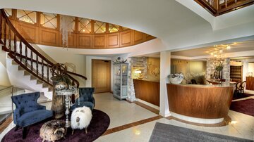 An elegant reception area with a curved staircase and stylish seating. The warm wooden tones and decorative elements create an inviting atmosphere.