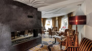 A stylish living room with a modern fireplace and elegant furniture. The windows are adorned with curtains and the carpet has an appealing design.