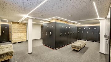 A modern changing room with black lockers and comfortable seating areas. The lighting is bright and creates an inviting atmosphere.