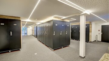 A modern changing area with several black lockers on a gray floor. The lighting is bright and creates an inviting atmosphere.