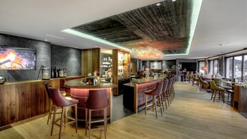 An elegant bar with wooden interiors and a cozy atmosphere. Bright lighting and a fireplace create an inviting ambiance.