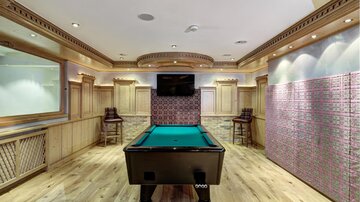 A stylish game room with a pool table in the center. In the background, a television and modern seating options can be seen.
