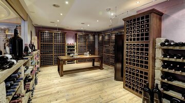 An elegant wine cellar with wooden shelves and a large selection of wines. The room is brightly lit and has a warm, inviting charm.