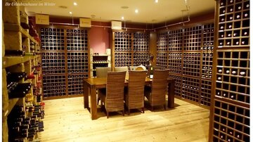 A stylish wine cellar with wooden walls and shelves full of wine bottles. In the middle stands a table with chairs, creating an inviting atmosphere.