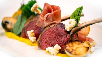 An artfully arranged dish with lamb chops, surrounded by fresh herbs and colorful side dishes. The presentation is refined and appetizing.