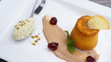A light dessert consisting of a colorful cupcake, a scoop of ice cream, and a cream. It is garnished with cherries and a slice of lemon.