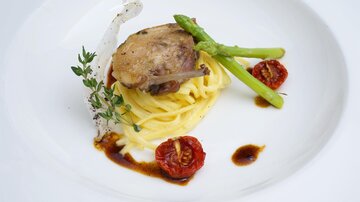 An elegant dish with pasta, tender meat, and fresh vegetables. The presentation is complemented by dried tomatoes and herbs.