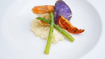 An artistic dish with shrimp, vegetables, and mashed potatoes. Colorful crackers and fresh vegetables complement the presentation.