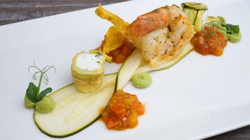 An elegantly arranged dish with a portion of shrimp and various vegetables. The dish is decorated with sauces and garnishes.