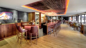 A modern bar with wooden interiors and cozy seating. The lighting creates an inviting atmosphere.
