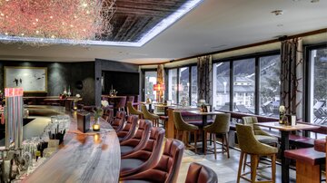 An elegant bar with a long counter and comfortable seating area. Large windows offer a view of the surroundings.