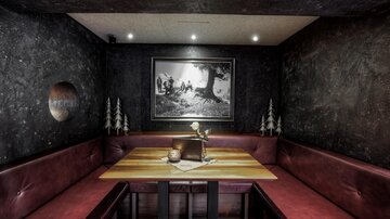 A stylish restaurant with a cozy seating area in dark tones. A black and white picture hangs on the wall, and the table is adorned with a small decoration.