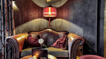 A cozy seating area with an elegant leather sofa and decorative pillows. A stylish lamp and a table create an inviting atmosphere.