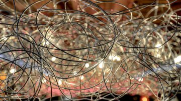 A tangled network of wire loops with warm light in the background. The structure creates an interesting and modern atmosphere.