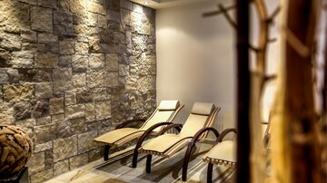 A relaxing room with loungers and a stone wall. The lighting creates a calm atmosphere.