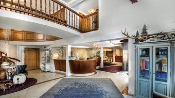 A spacious reception hall with wooden details and an elegant reception desk. The design is modern and inviting, with a beautiful carpet in the foreground.