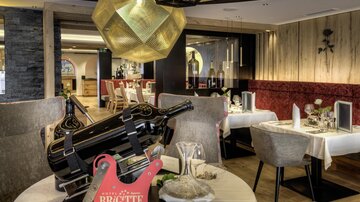 An elegant restaurant with stylish tables and a striking lamp. A large bottle of wine is on the table, and decorations are carefully arranged.