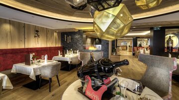 An elegant restaurant with stylish tables and modern lamps. In the foreground, there is a bottle of wine in a striking holder.