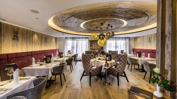An elegant restaurant with stylish tables and comfortable chairs. The warm wooden ceiling and soft lighting create an inviting atmosphere.