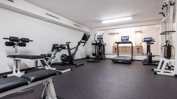 A modern gym with various workout machines. It is well-lit and carpeted.