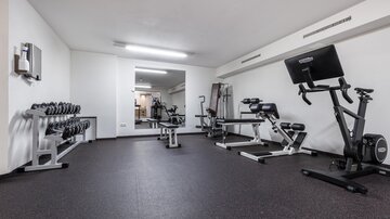 A simple gym with various training equipment. There are weights, a bench, and a stationary bike in a modern space.