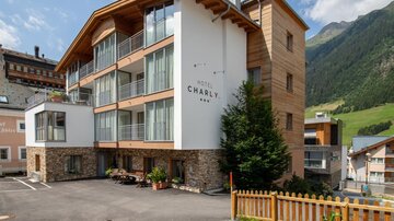 A modern hotel building with a wooden and stone facade. Surrounded by mountains and a green landscape.