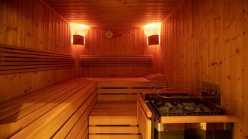 A cozy sauna with a wooden bench and pleasant lighting. The sauna stove is ready to provide warmth.