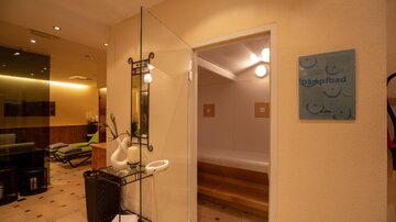 An inviting entrance to a wellness area with a glass portal door. The walls are in warm colors, and there are modern lighting elements.