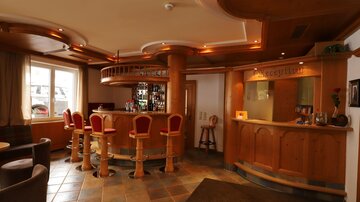 An inviting bar with wood paneling and red bar stools. The room is well-lit and offers a cozy atmosphere.