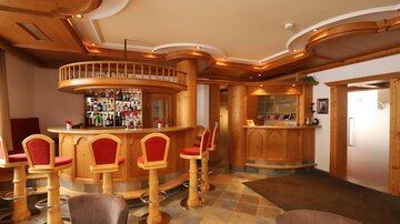 A cozy bar with wooden decor and red bar stools. The area is well-lit and invites you to linger.