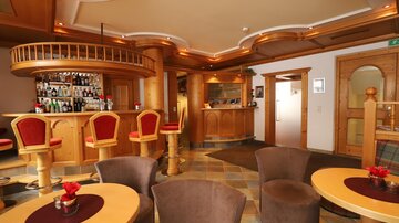 A cozy bar area with wooden decor and red chairs. In the background, there is a well-stocked bar.