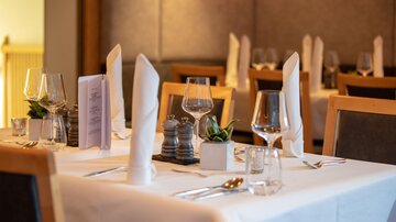 An elegantly set table in a restaurant with cutlery, glasses, and decorative elements. The tablecloth is white and the atmosphere is cozy and inviting.