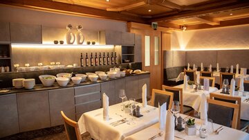 An elegant restaurant with beautifully set tables and a buffet area. The atmosphere is inviting and modern.