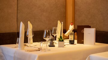 An elegantly set table in a restaurant. This includes glasses, a bottle of wine, and a menu.