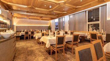 An elegant restaurant with wooden elements and soft lighting. The tables are neatly set and ready for guests.