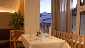 A stylish restaurant table with a white tablecloth and elegant glasses. In the background are snow-capped mountains and large windows that let in plenty of light.