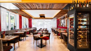 Ein modernes Restaurant mit elegante Einrichtung und gemütlichen Tischen. Große Fenster sorgen für viel Licht und eine einladende Atmosphäre.