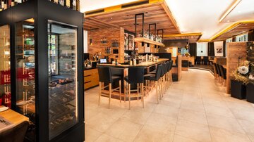 Eine moderne Bar mit stilvollem Holzinterieur und einer einladenden Atmosphäre. Im Hintergrund sind Regale mit Getränken und Sitzgelegenheiten für Gäste zu sehen.