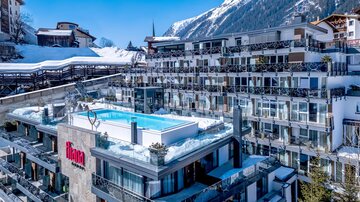 A modern hotel with a rooftop terrace and a pool, surrounded by snow-capped mountains. The facilities appear inviting and stylish.