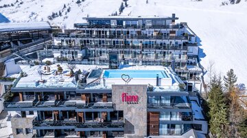 A modern hotel in the mountains with an outdoor pool and balconies. The snow around the building creates a lovely winter atmosphere.