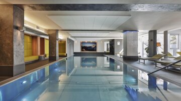An elegant indoor pool with clear water and modern design. The space is furnished with comfortable loungers and stylish amenities.