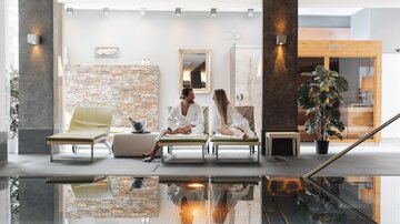 An elegant wellness area with loungers and a water basin. Two women in bathrobes relax and enjoy the harmonious atmosphere.