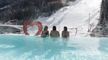 A warm pool overlooking a snow-covered slope. Three people are enjoying the view in a relaxed atmosphere.