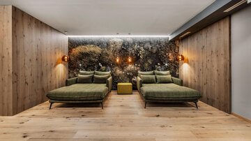 A modern relaxation room with two green loungers and warm wooden details. The wall is decorated with a naturalistic planting, creating a calming atmosphere.
